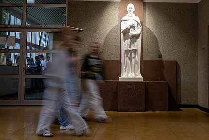 Eine große Schlange aus Schülerinnen und Schüler gehen zusammen mit ihren Eltern durch einen Eingang des Gebäudes.