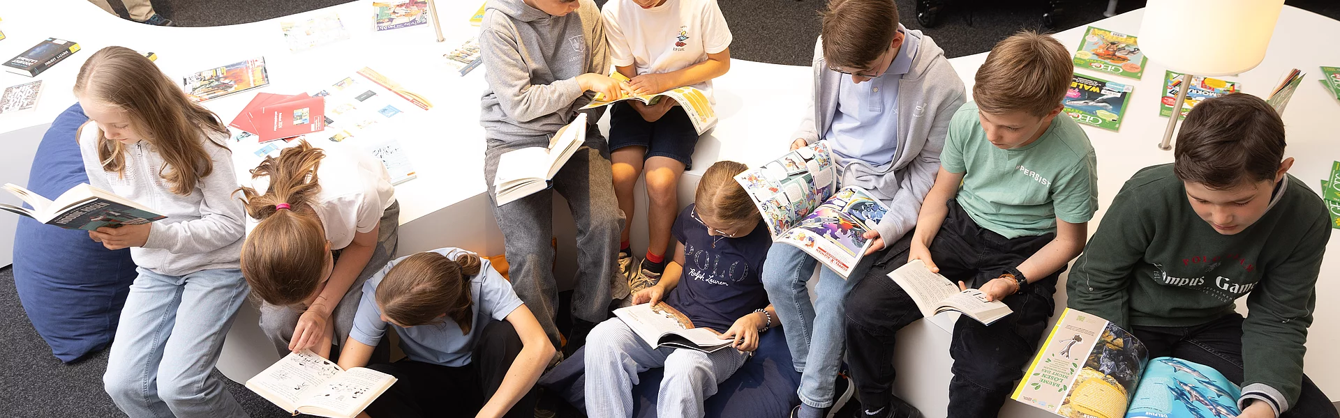 Schülerinnen und Schüler sitzen nebeneinander schauen in die Kamera und haben alle ein Buch, oder eine Zeitschrift in der Hand.