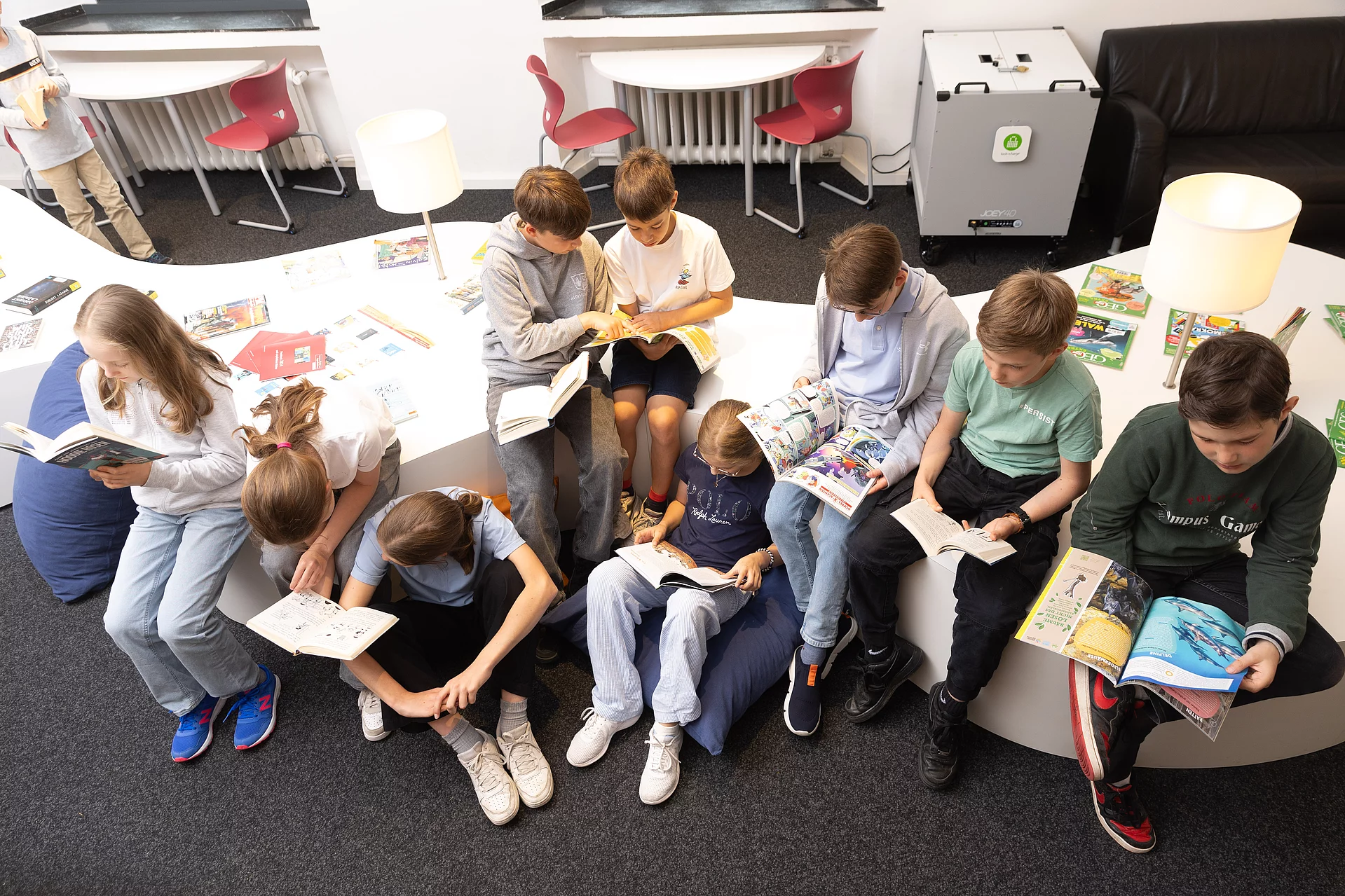 Schülerinnen und Schüler sitzen nebeneinander schauen in die Kamera und haben alle ein Buch, oder eine Zeitschrift in der Hand.