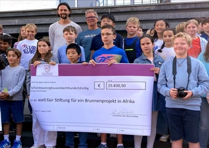 Schülerinnen und Schüler stehen zusammen und halten einen großen Scheck in der Hand, welcher mit 25.830,50€ and die well:fair Stiftung geht für ein Brunnenprojekt in Afrika.