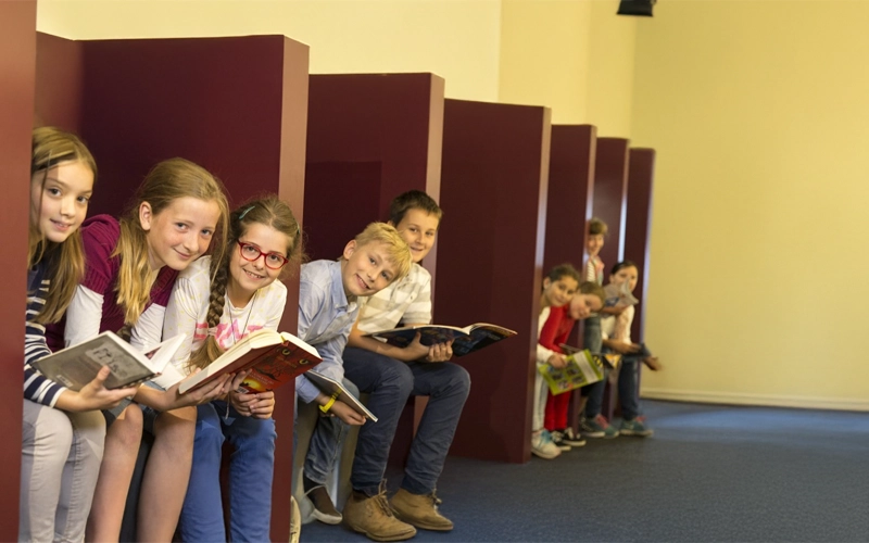 Schülerinnen und Schüler sitzen nebeneinander schauen in die Kamera und haben alle ein Buch, oder eine Zeitschrift in der Hand.